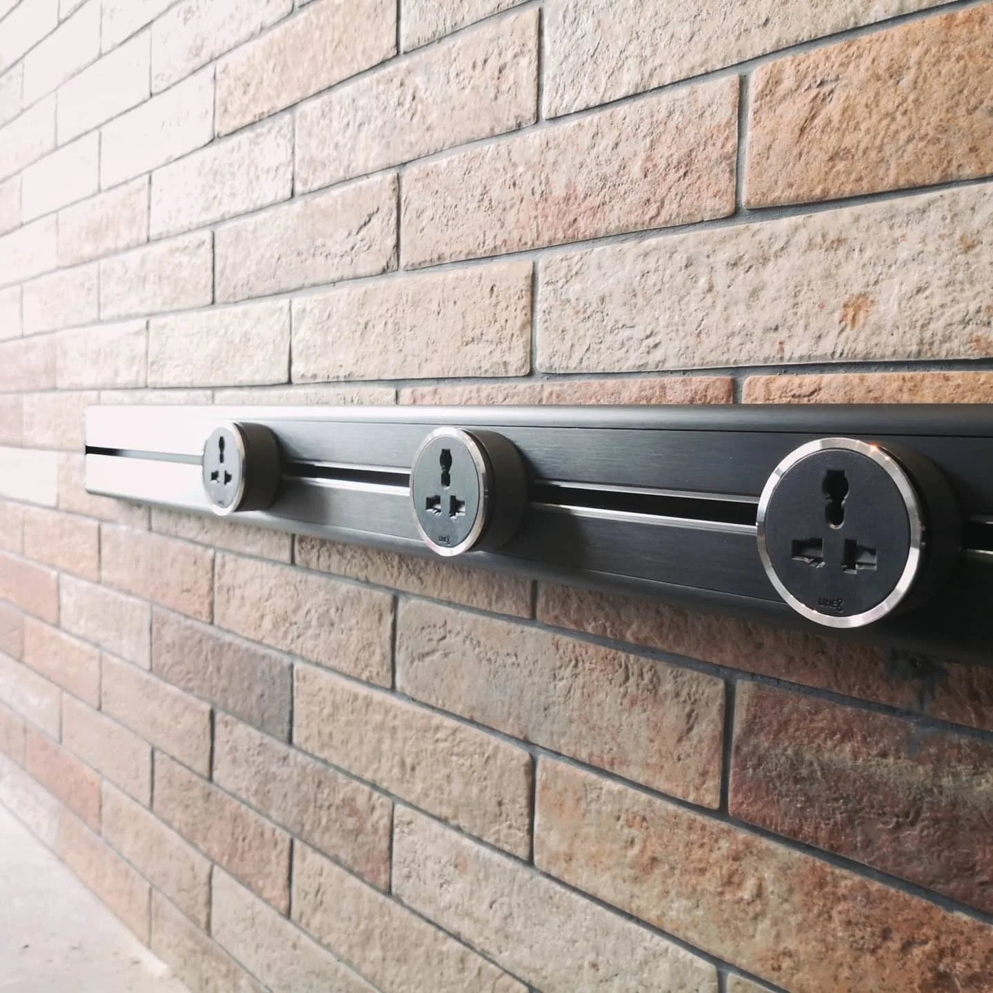 Line8 Model SL track in Black Hairline mounted on a brick wall with power outlets
