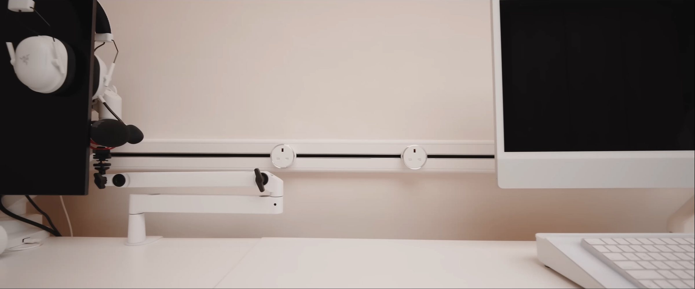 White Line8 adaptors on a power track behind two monitors on a home office desk with a monitor arm and headset