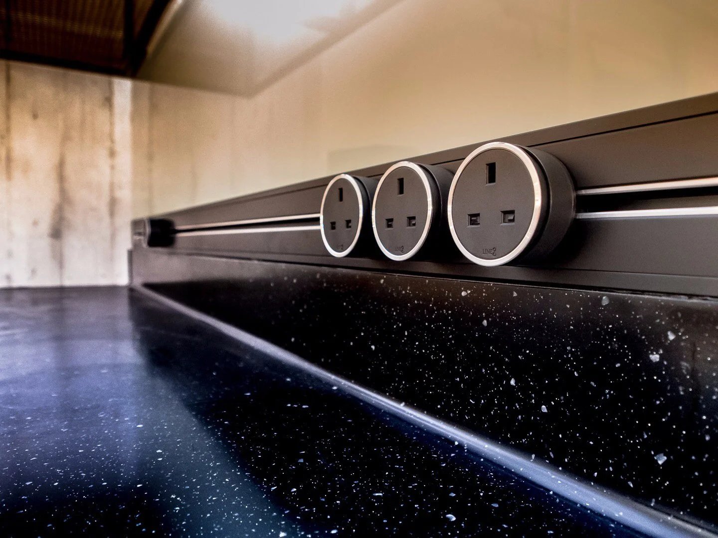 Line8 Model SL track in Black Hairline above a black countertop with power outlets
