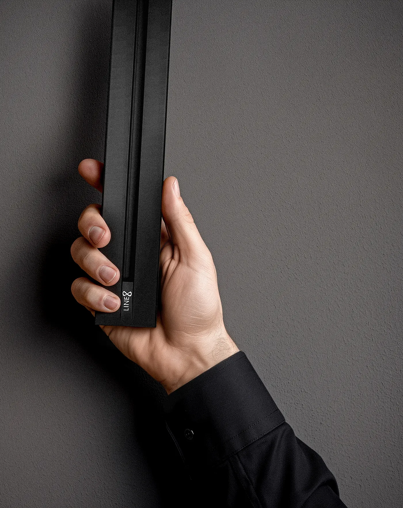 Hand holding the Line8 Zen Track power track, revealed against a dark wall, showing the LINE8 logo on the end cap.