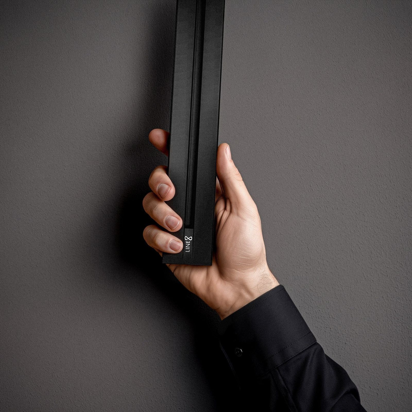 Hand holding the Line8 Zen Track power track, revealed against a dark wall, showing the LINE8 logo on the end cap.